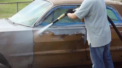 Abrasive blasting being used to remove coating from a vehicle